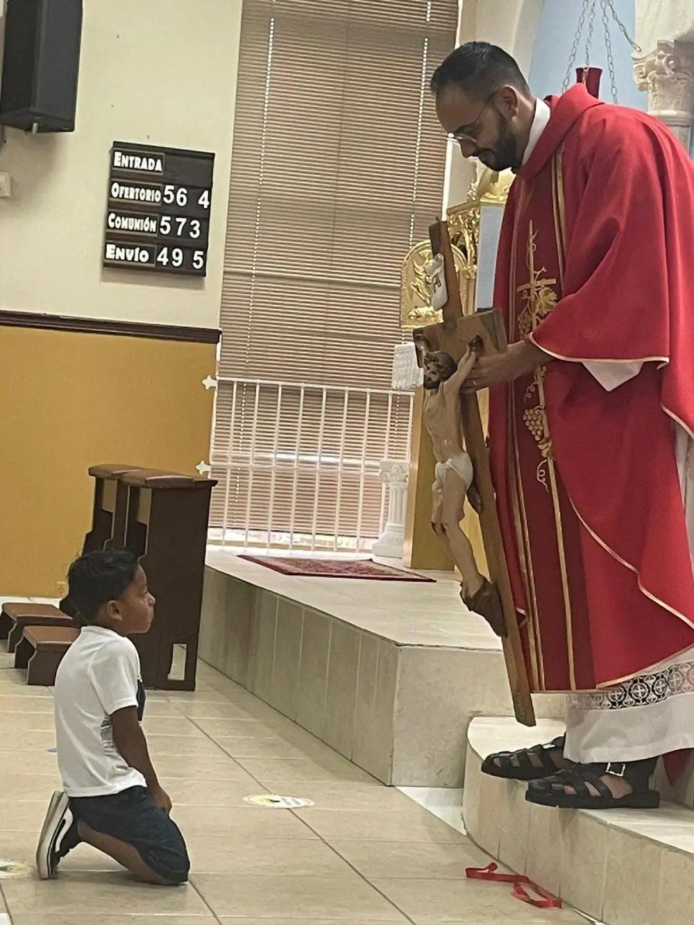 A priest holding a cross in front of a kneeling child